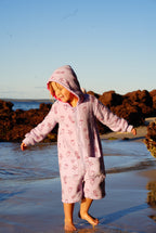 Child wearing lilac hooded towel jumpsuit that is made from organic cotton and designed to prevent trips and falls around water